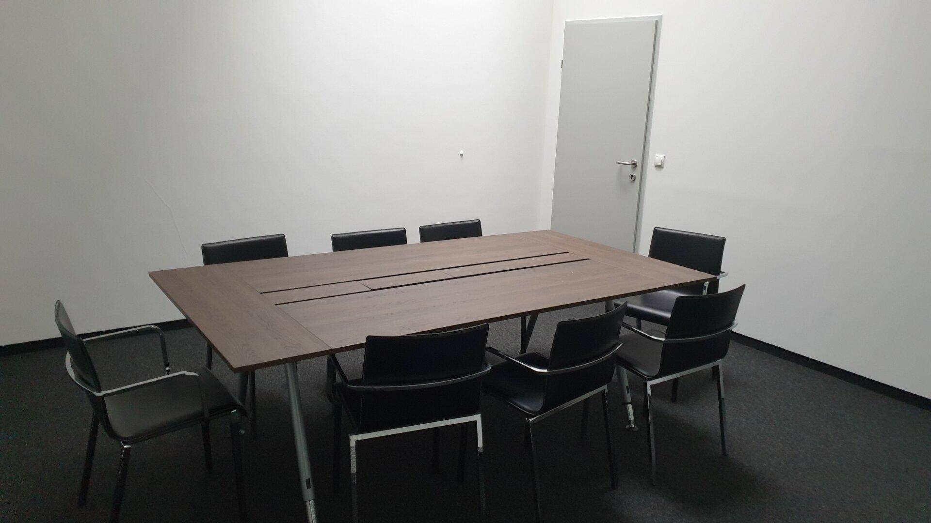 Konferenzraum mit großem Holztisch und schwarzen Stühlen, ideal für Besprechungen.