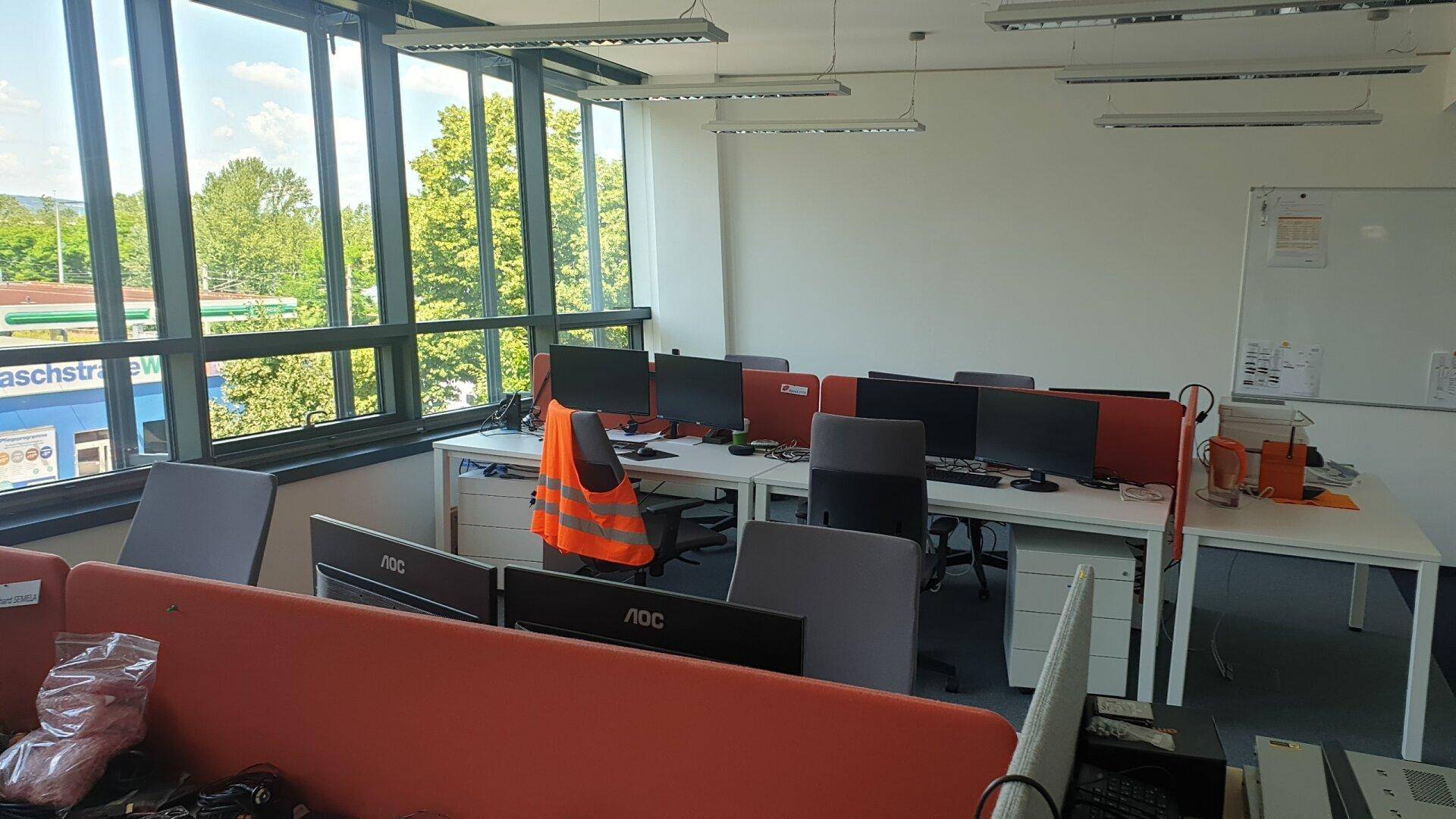 Helles Büro mit zahlreichen Arbeitsplätzen und großen Fenstern, die viel Tageslicht hereinlassen.