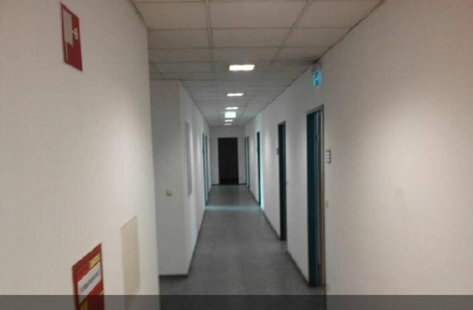 Langer, heller Flur mit weißen Wänden, mehreren Türen und Deckenbeleuchtung.