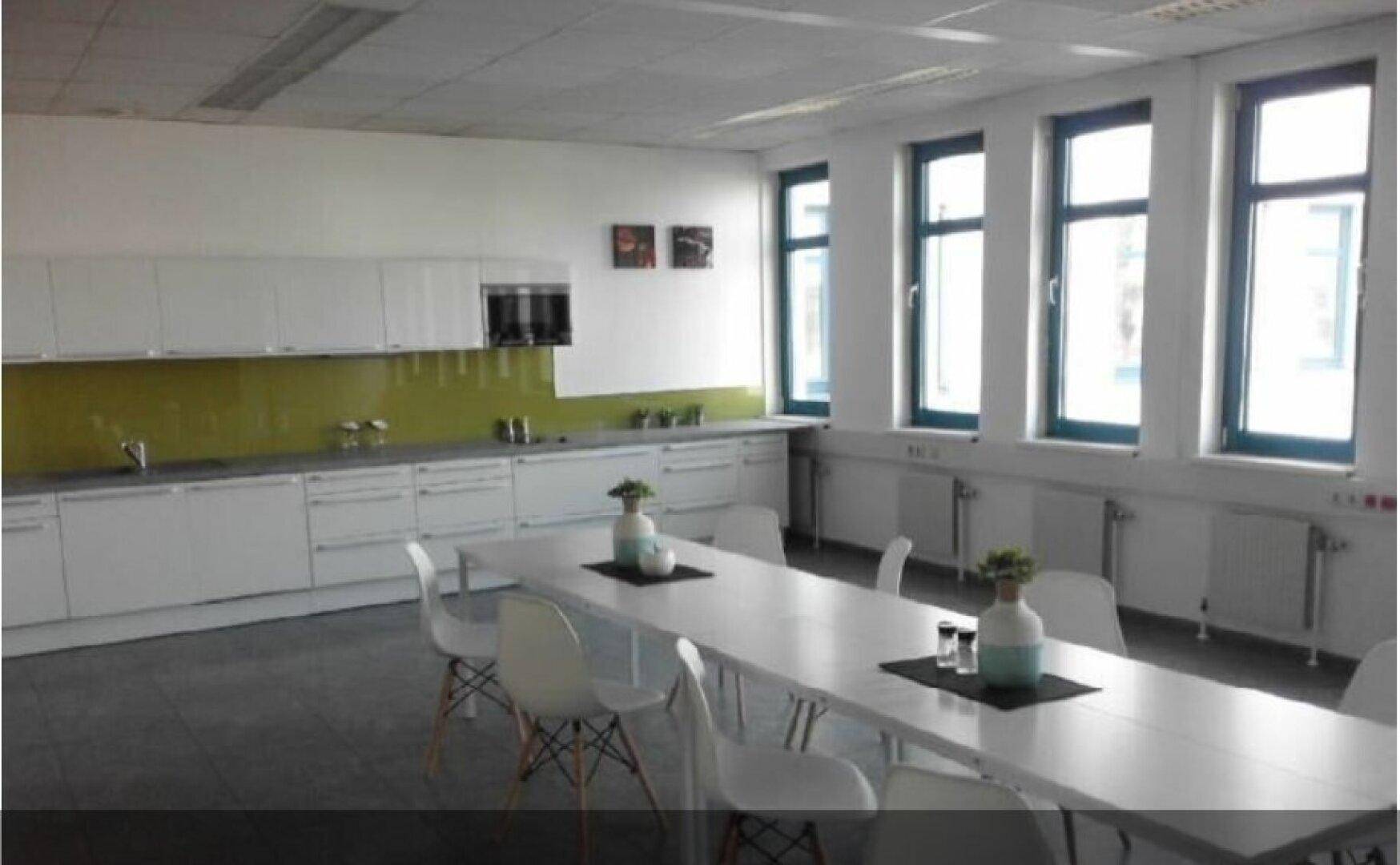 Moderne Küchenzeile mit weißer Einrichtung, langer Esstisch und großen Fenstern.