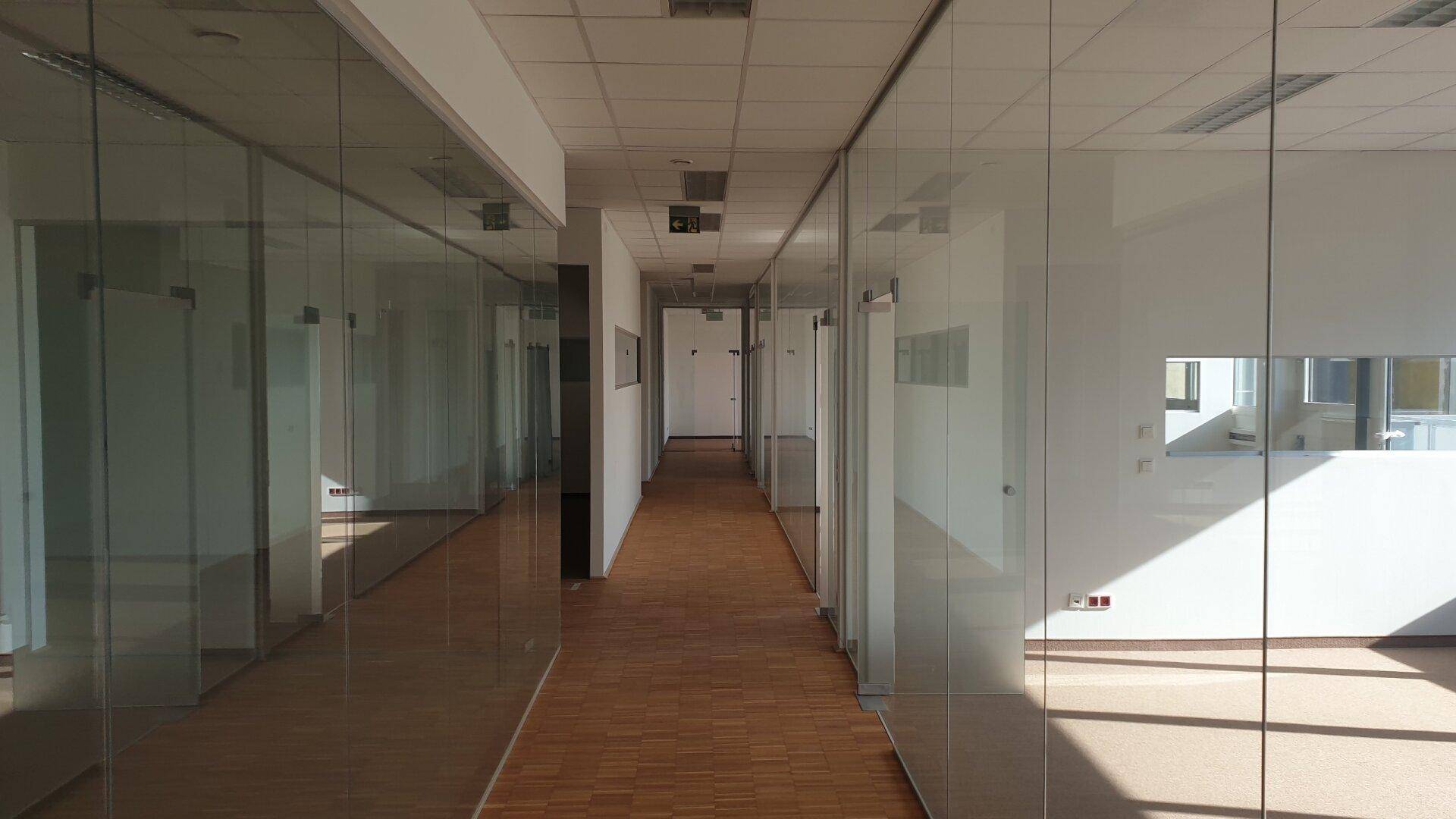 Heller Bürogang mit Glaswänden zu den einzelnen Büros und Holzparkettboden.
