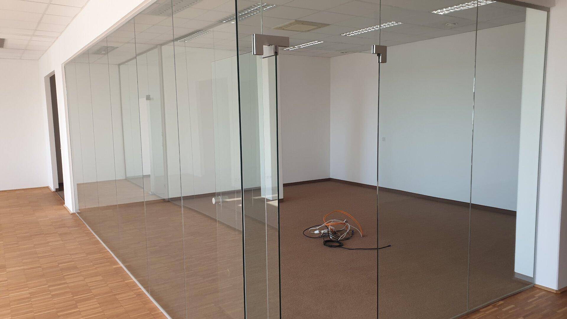 Modernes Büro mit Glaswänden, Teppichboden und Blick auf den Flur.