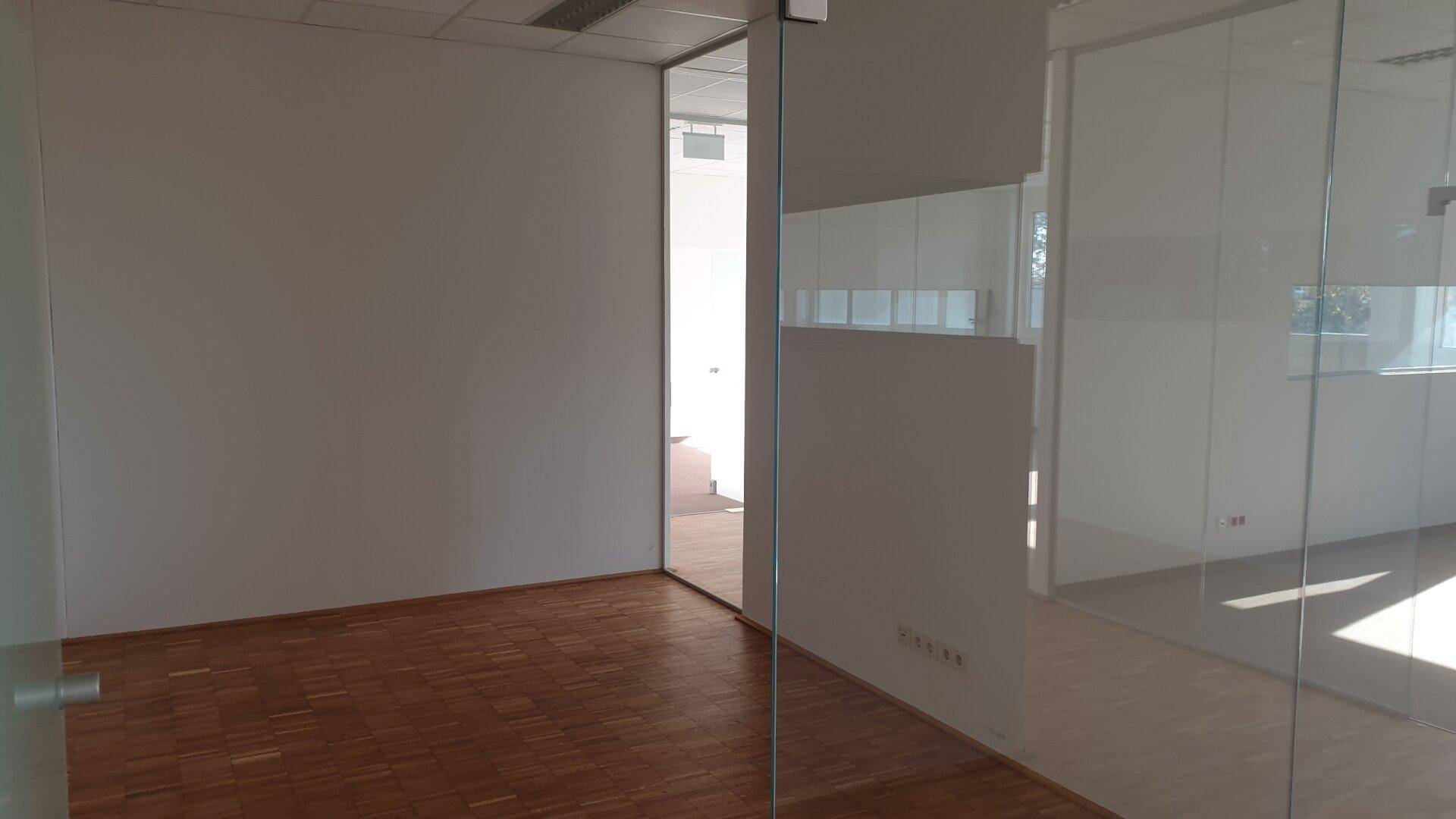 Büro mit Holzparkettboden und einer Glaswand, die den Raum hell und offen wirken lässt.