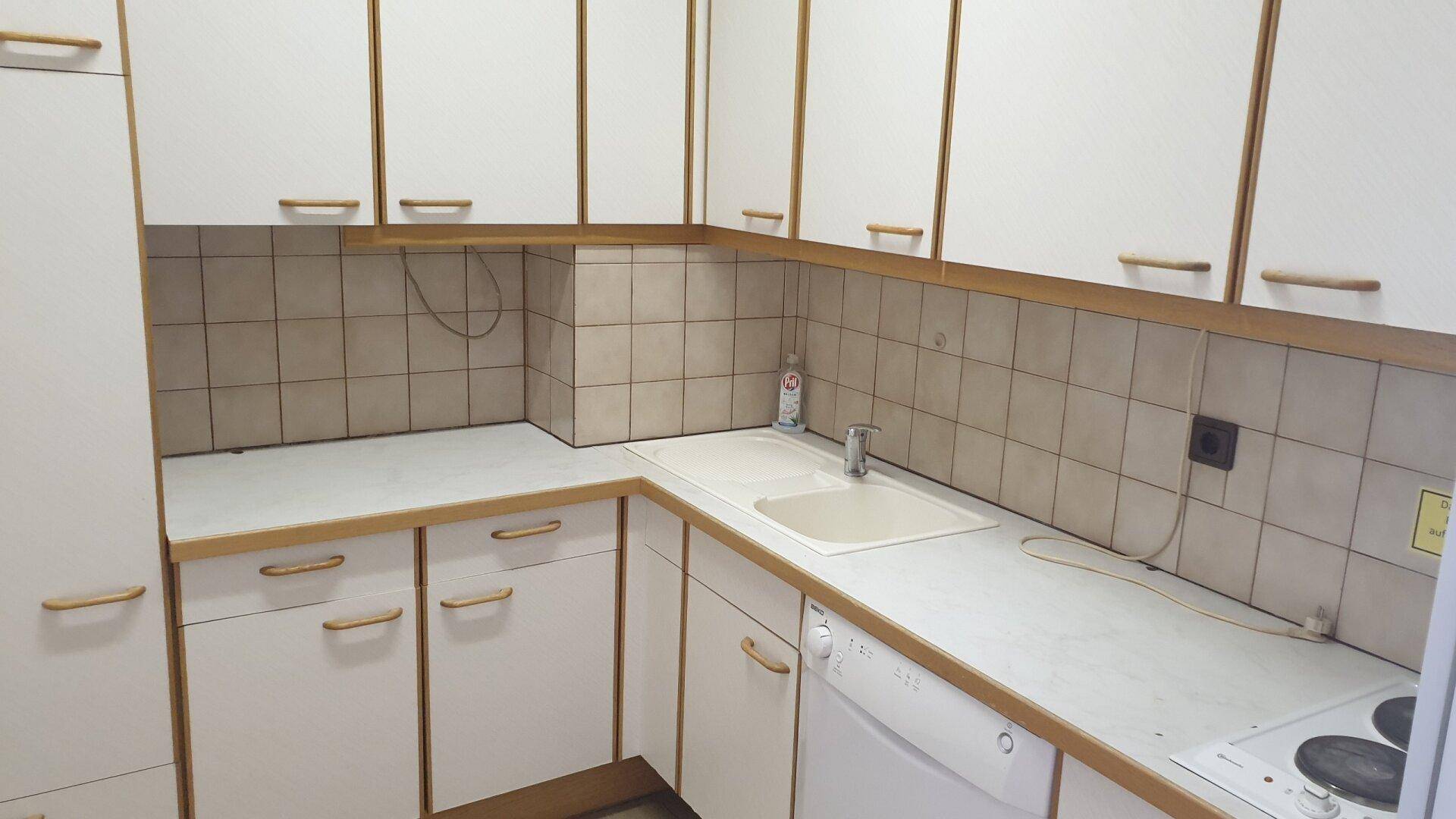 Funktionale Küche mit weißen Schränken, beigen Fliesen und einem Elektroherd.