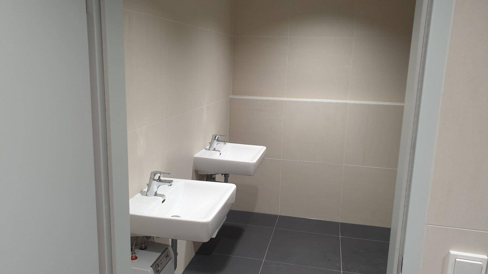 Helle Toilette mit zwei Waschbecken und beigen Wandfliesen.