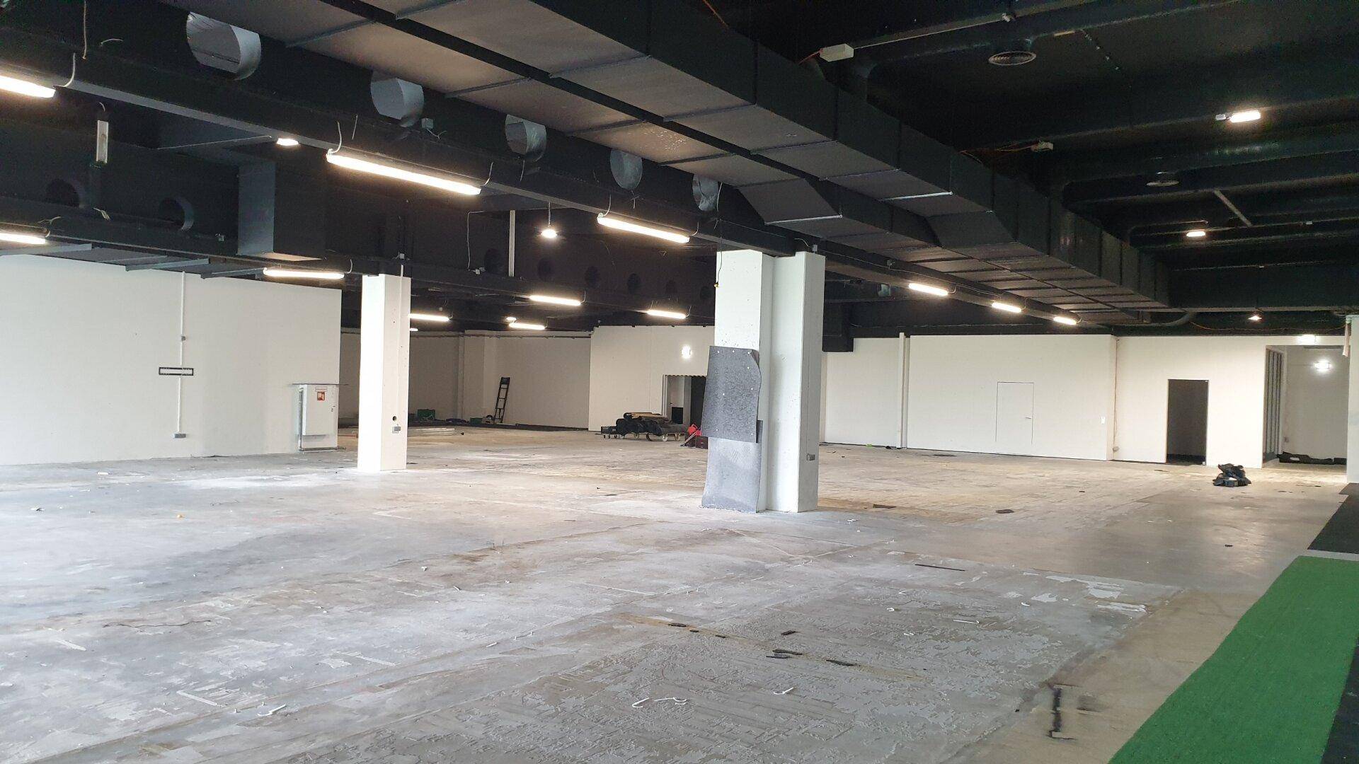 Großer, leerer Gewerberaum mit Betonboden, hohen Decken und sichtbaren Lüftungsrohren, ideal für individuelle Gestaltung.