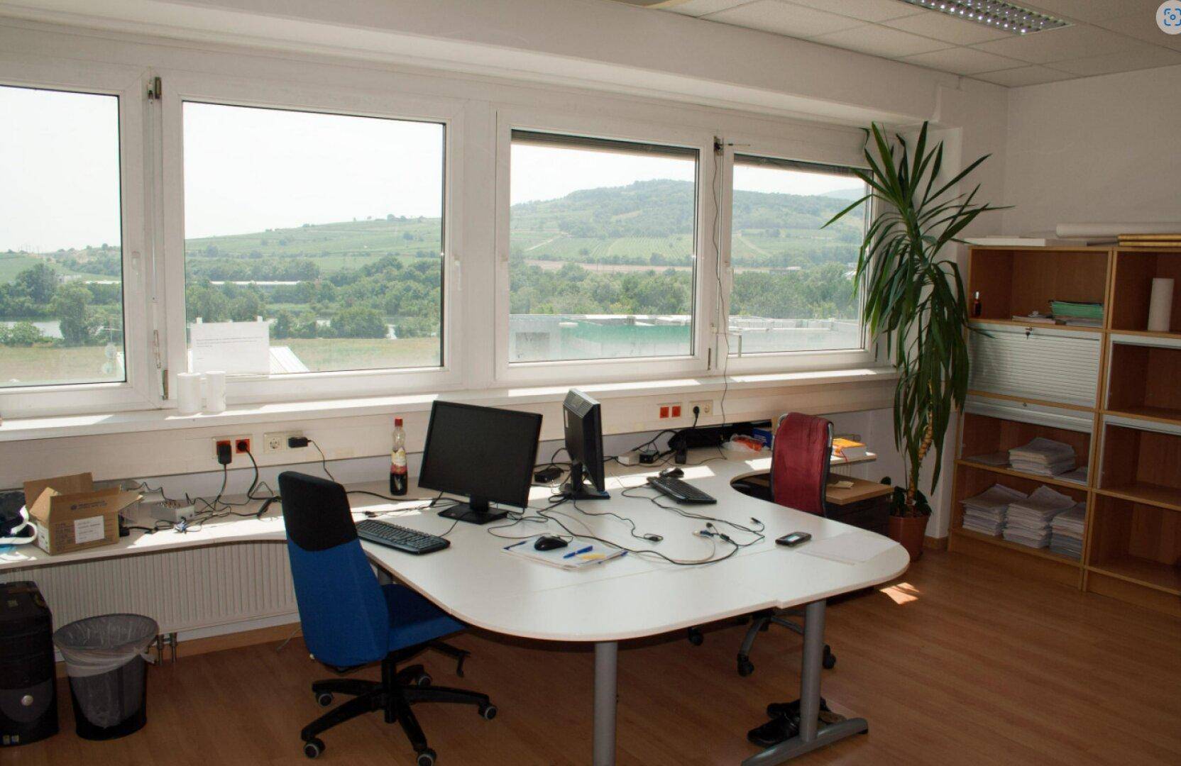 Funktionaler Büroraum mit Schreibtisch, Laminatboden und weitem Blick auf die Landschaft.