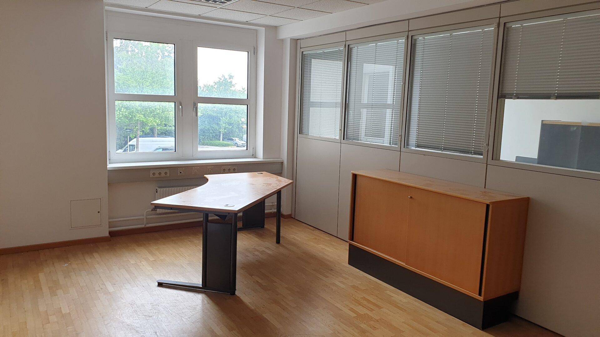 Geräumiges Büro mit Holzfußboden, großen Fenstern und einfacher Büroeinrichtung.