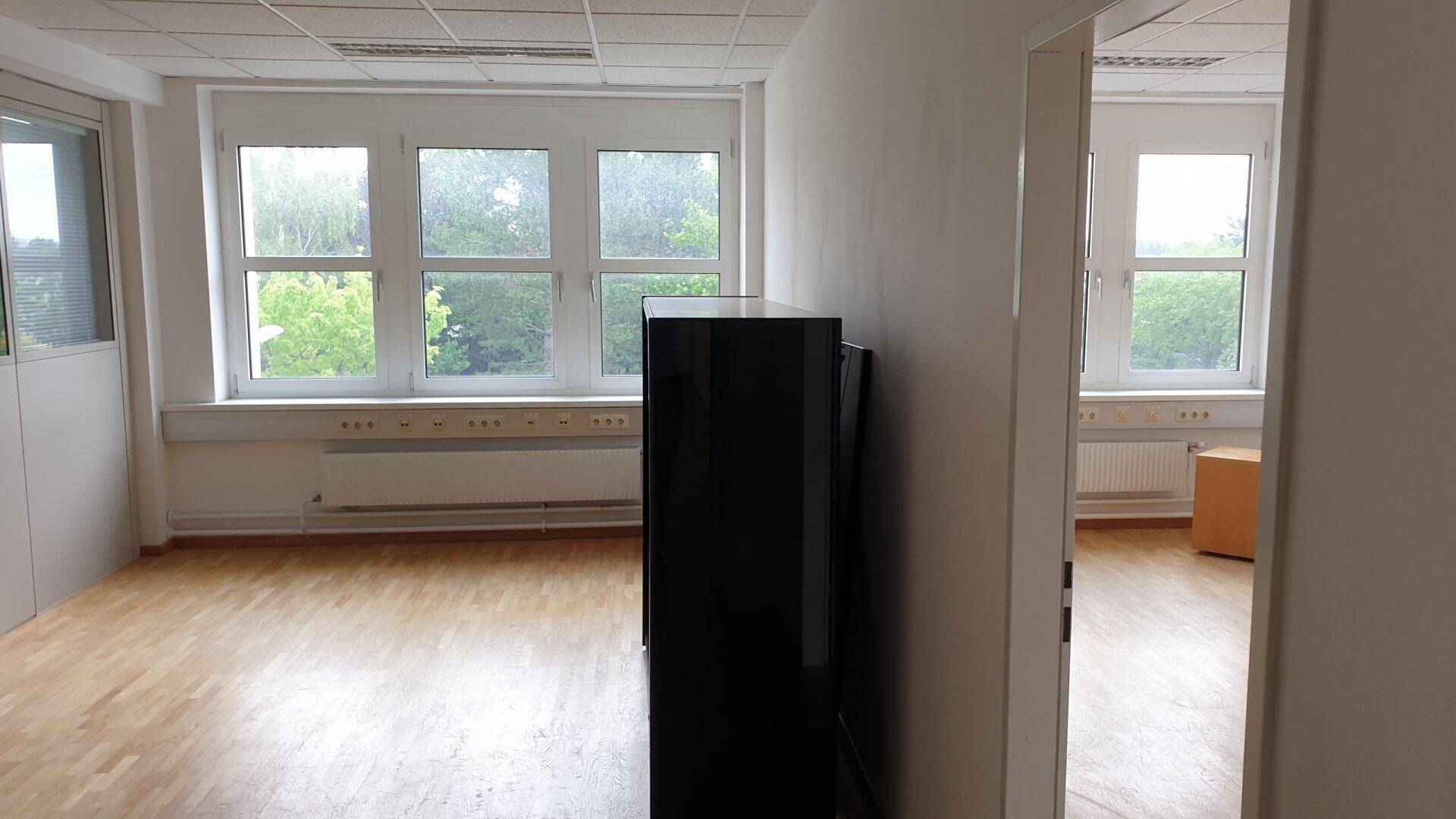 Helles Büro mit Holzfußboden und mehreren Fenstern, die einen Blick ins Grüne bieten.