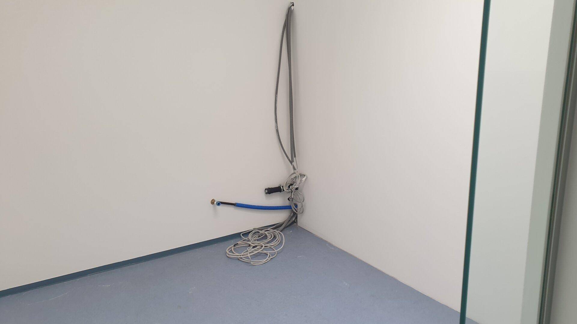 Leere Ecke eines Raumes mit weiß gestrichenen Wänden, blauem Boden und sichtbaren Kabeln.