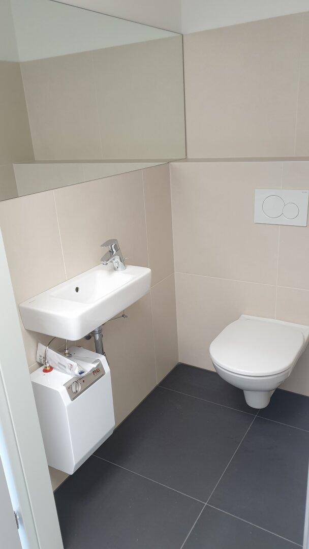 Modernes WC mit wandhängender Toilette, kleinem Waschbecken und dunklen Fliesen auf dem Boden.