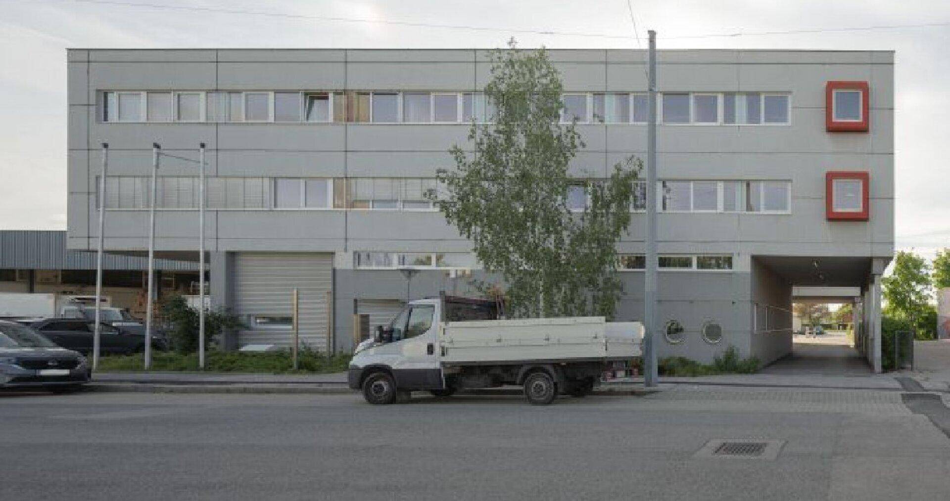 Modernes Geschäftsgebäude mit grauer Fassade, großen Fenstern und einem Durchgang im Erdgeschoss.