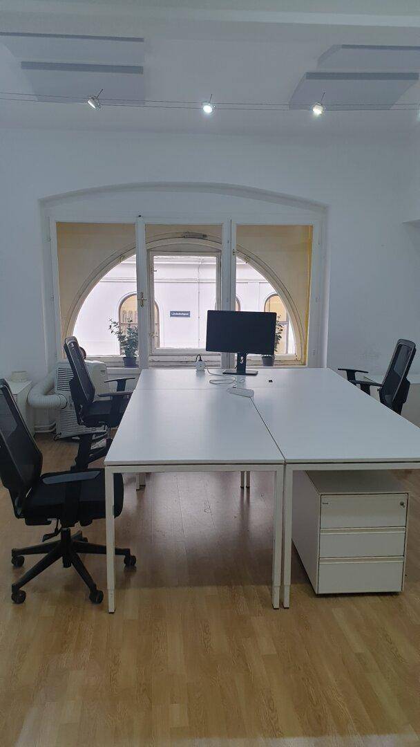 Geräumiges Büro mit mehreren Arbeitsplätzen, modernen Möbeln und charakteristischen Bogenfenstern, die den Raum erhellen.