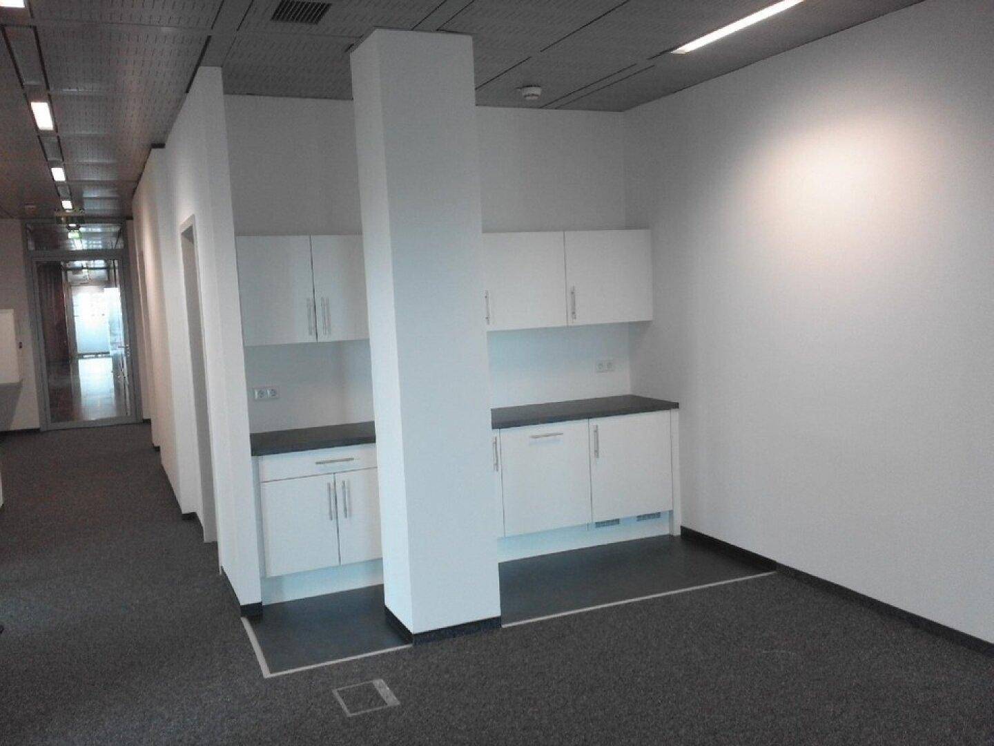 Kleine, funktionale Teeküche mit weißen Schränken und dunklen Arbeitsplatten in einem Bürobereich.