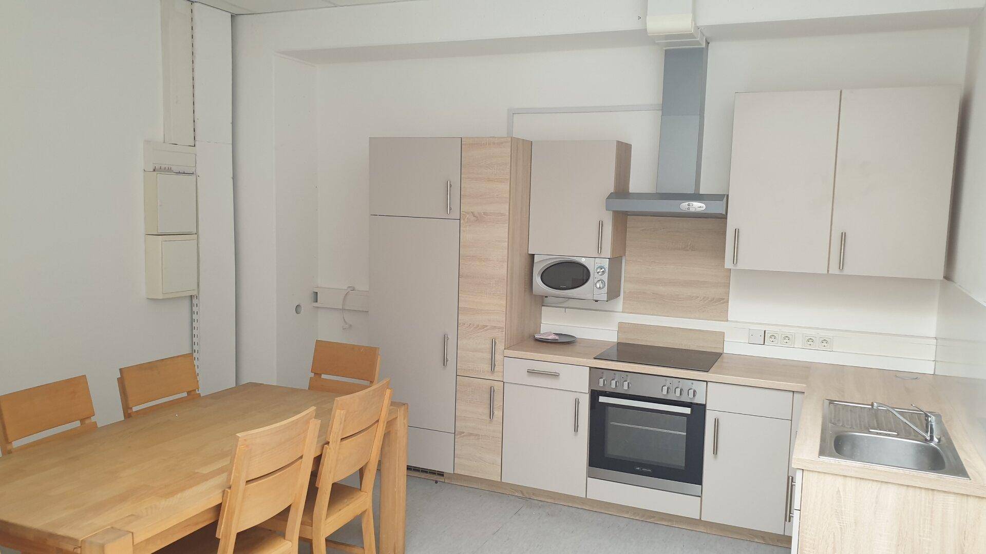 Funktionale Küche mit Essbereich, hellen Holzschränken, integrierten Geräten und Dunstabzugshaube.