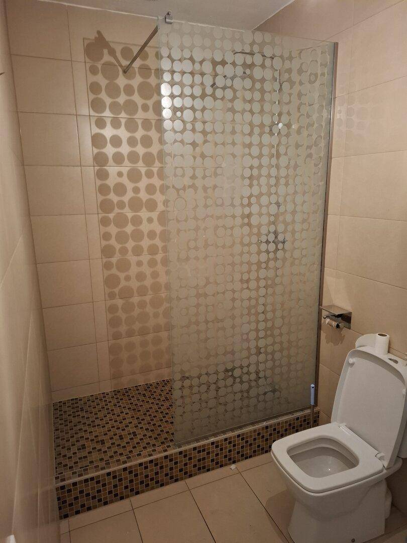 Modernes Badezimmer mit Duschkabine, WC und beigefarbenen Fliesen an Wänden und Boden.