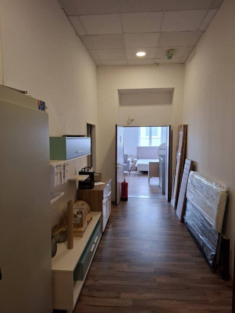 Langer Flur mit Holzfußboden, hohen Decken und Blick in einen weiteren Raum.
