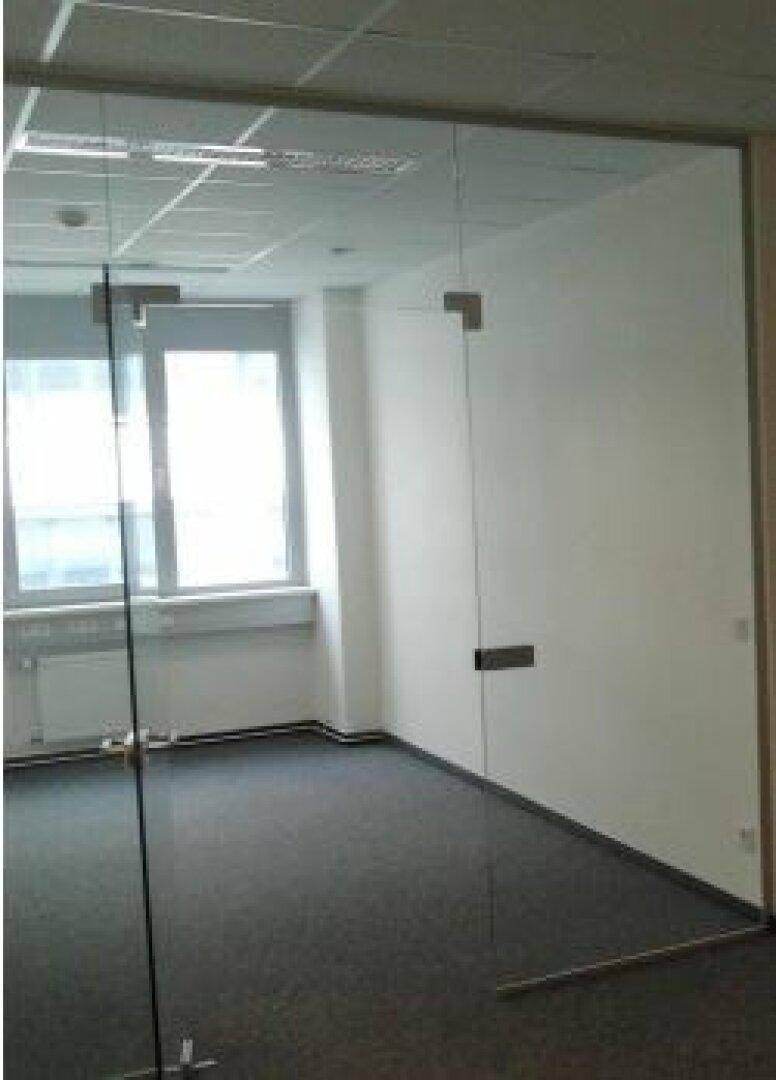Leeres Büro mit Teppichboden und Glaswänden, das viel Tageslicht durch die Fenster erhält.