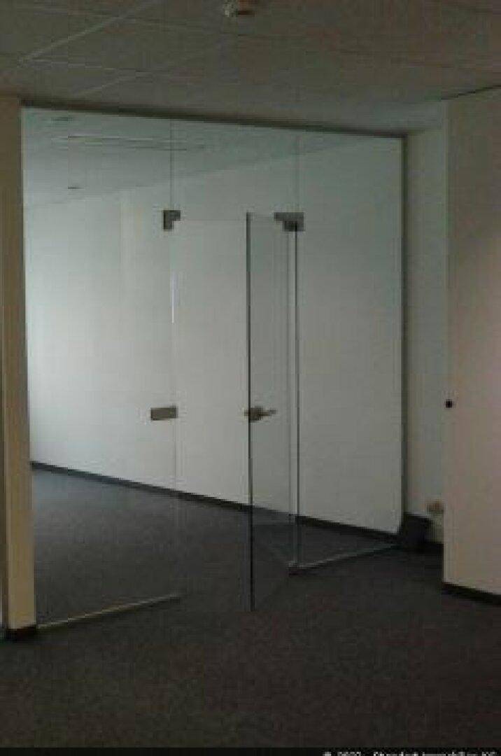 Leerer Büroraum mit Teppichboden und modernen Glastüren, die Transparenz schaffen.