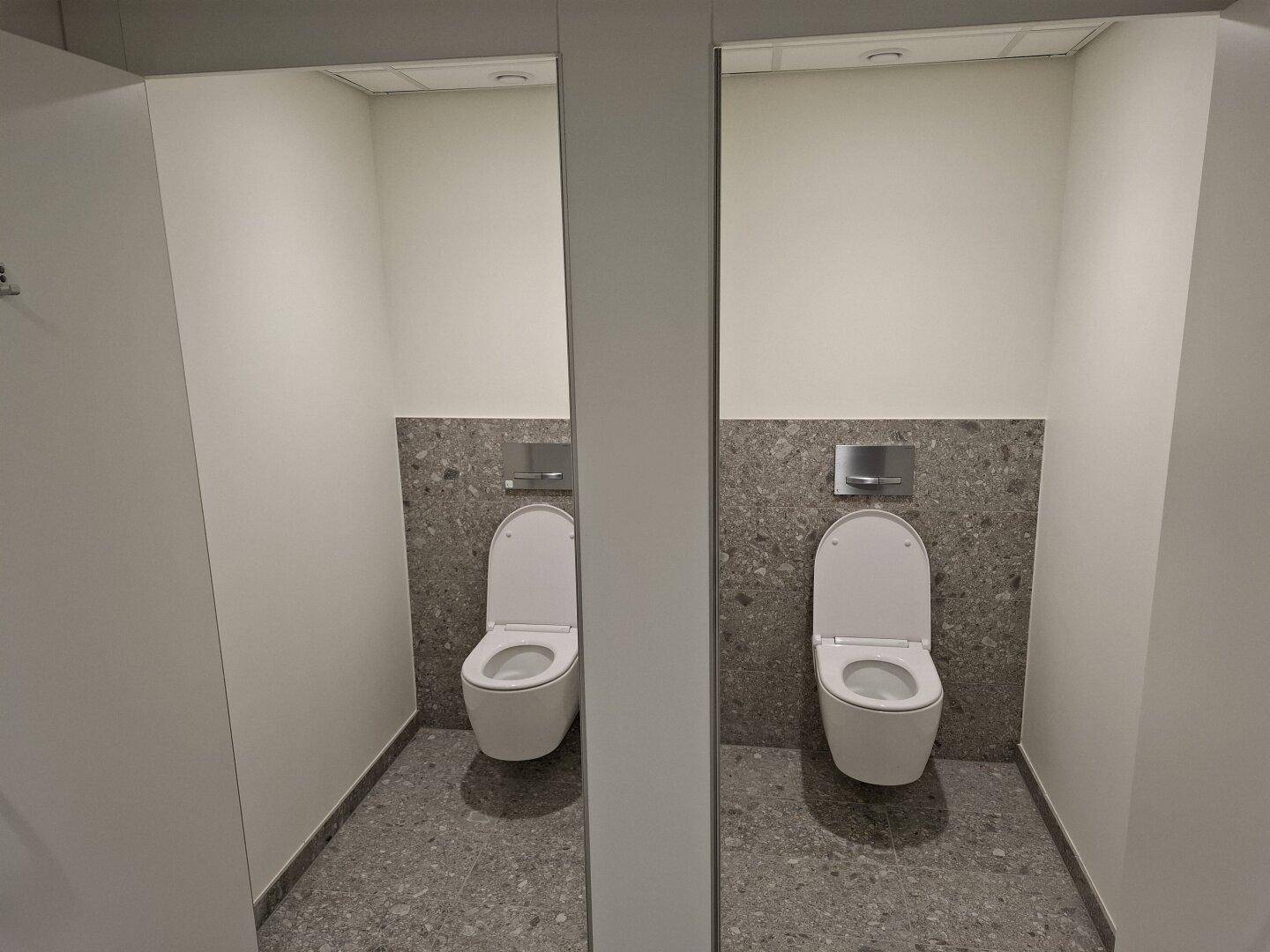 Zwei separate Toilettenkabinen mit modernen Wand-WCs und gefliesten Rückwänden.
