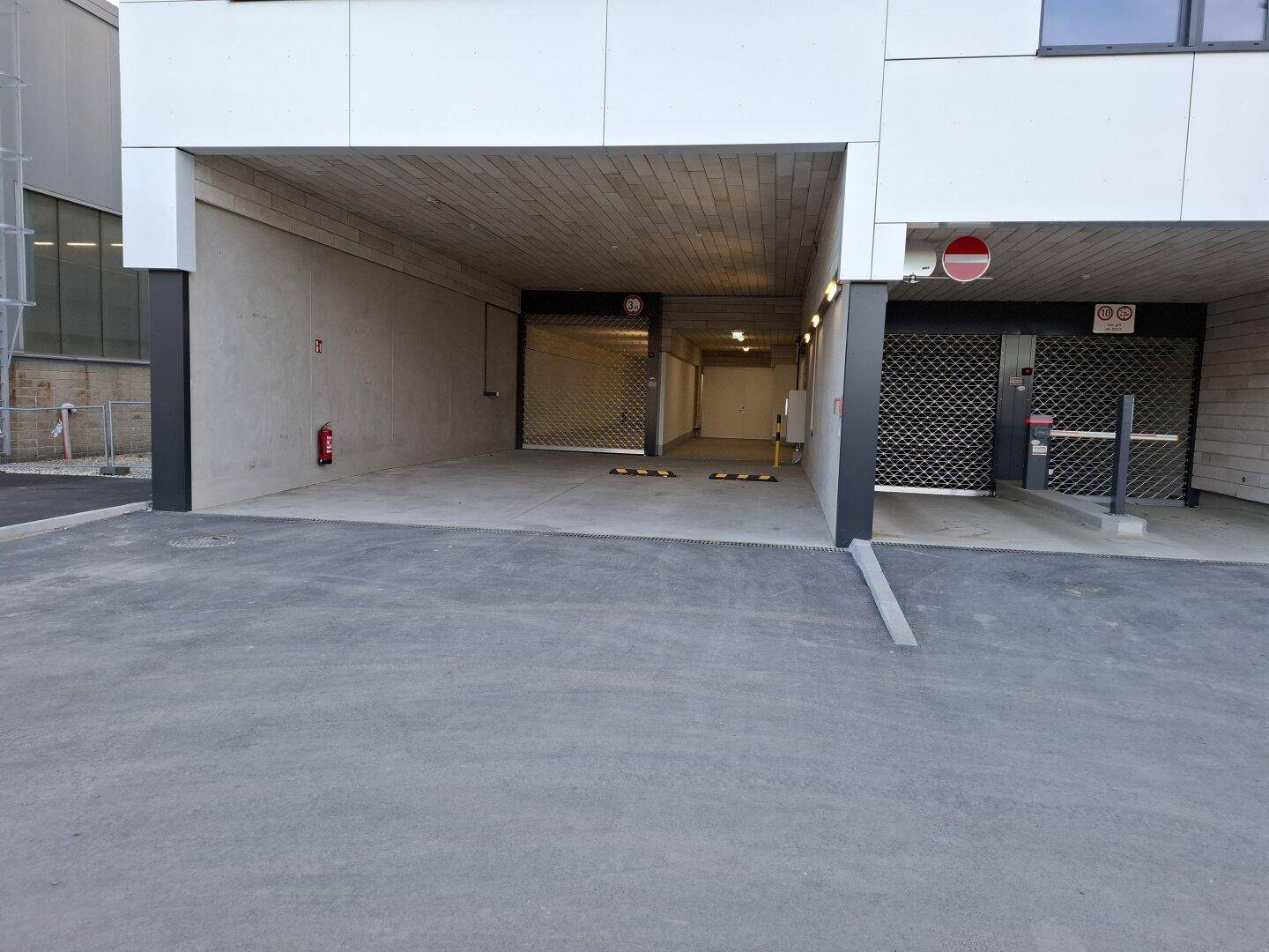 Einfahrt zu einer Tiefgarage mit zwei Rolltoren und einem modernen Gebäudeeingangsbereich.
