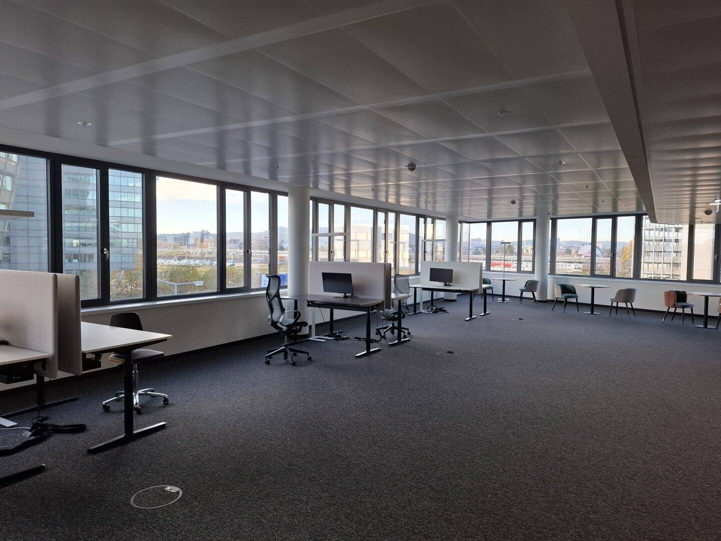 Geräumiger, offener Bürobereich mit zahlreichen Arbeitsplätzen und großen Fenstern mit Stadtblick.