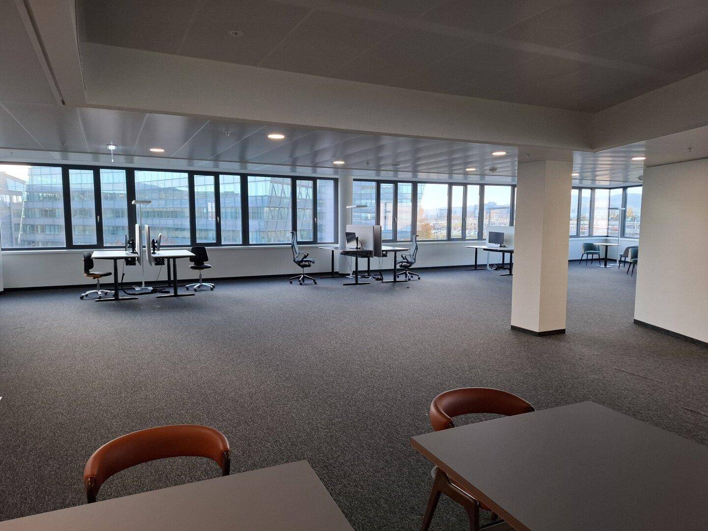 Weitläufiger, offener Bürobereich mit zahlreichen Arbeitsplätzen und großen Fenstern mit Stadtblick.
