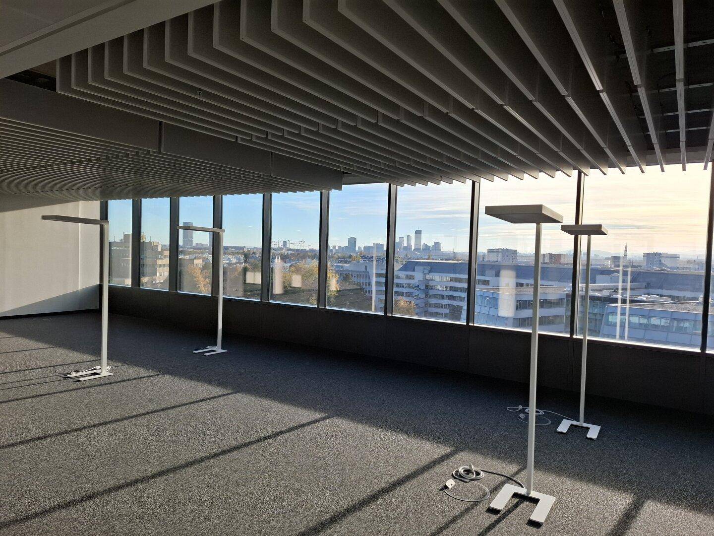 Offener Bürobereich mit Lamellendecke, großen Fenstern und Panoramablick auf die Stadt.
