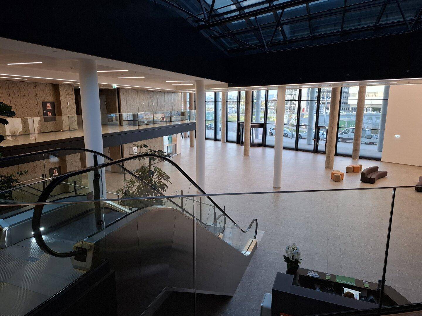 Geräumige, moderne Lobby mit Rolltreppe, hohen Decken und großen Glasfronten.