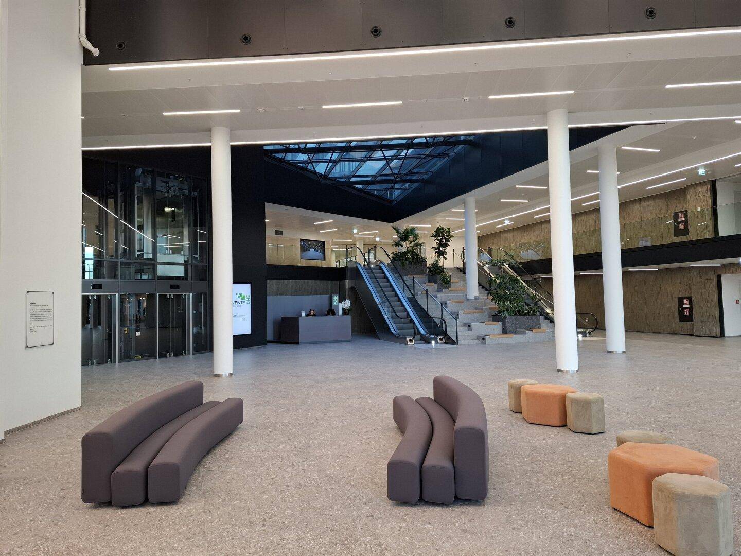 Moderne Lobby mit bequemen Sitzbereichen, Rolltreppen und einem weitläufigen, offenen Raumgefühl.
