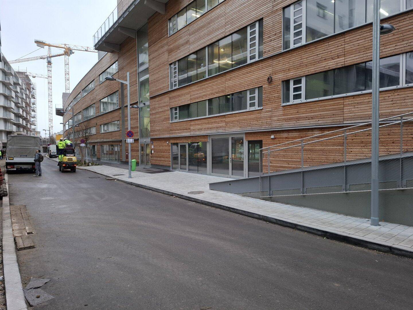 Moderne Holzfassade eines Neubaus mit großen Fenstern und Baustellenkränen im Hintergrund.
