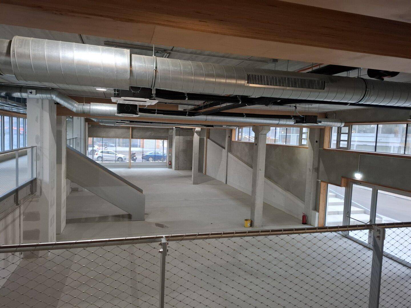 Großer, offener Gewerberaum im Rohbau mit sichtbaren Lüftungsrohren und Betonstützen.