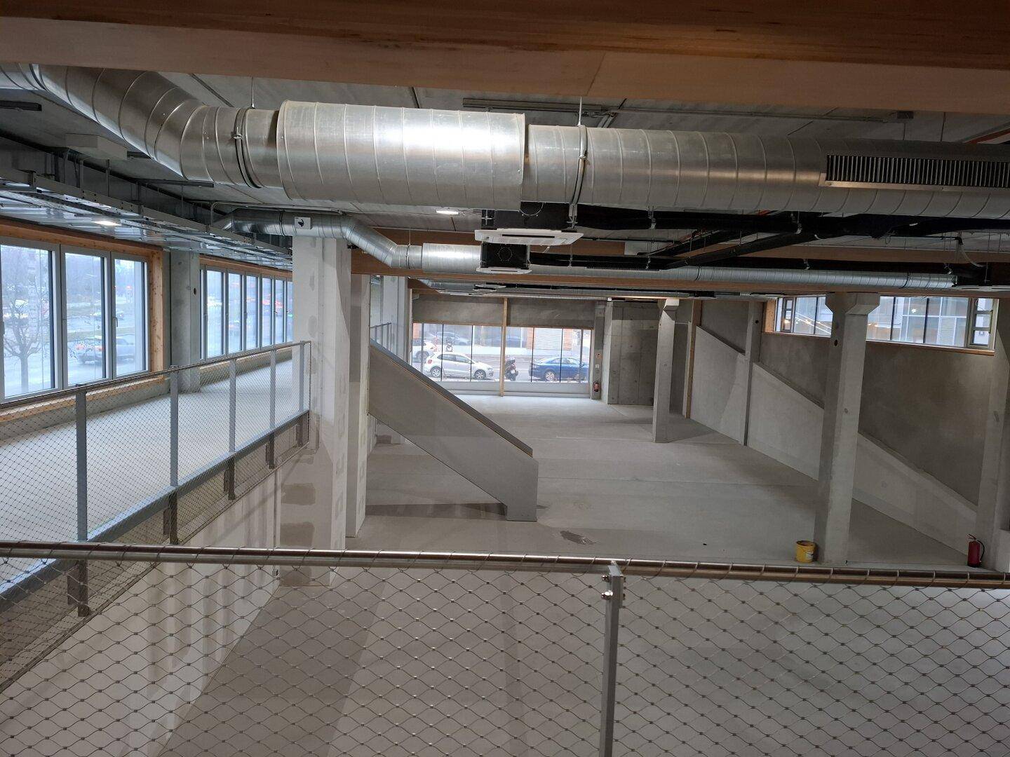 Geräumiger, unfertiger Innenraum mit großen Fenstern, sichtbaren Lüftungsanlagen und Betonstrukturen.