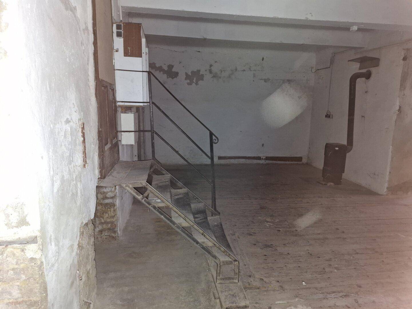 Blick auf eine Metalltreppe in einem großen, sanierungsbedürftigen Raum mit einem Ofen und sichtbaren Rohren.