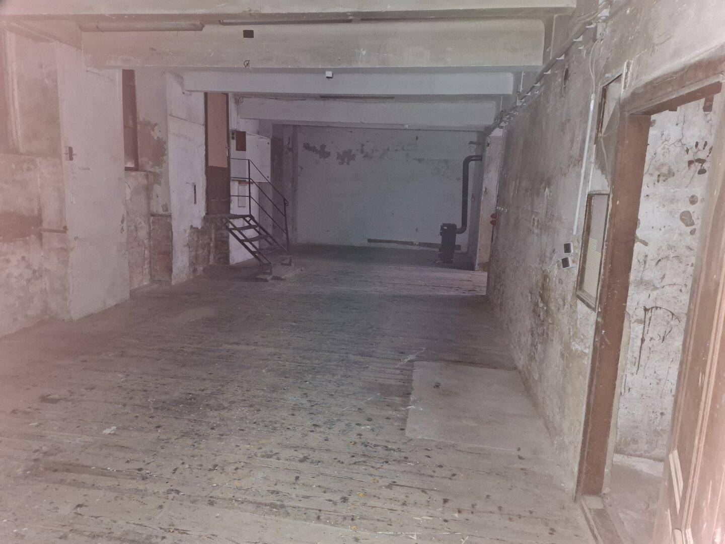 Weitläufiger Kellerraum mit einer Metalltreppe und abgenutzten Wänden, der auf eine umfassende Sanierung wartet.
