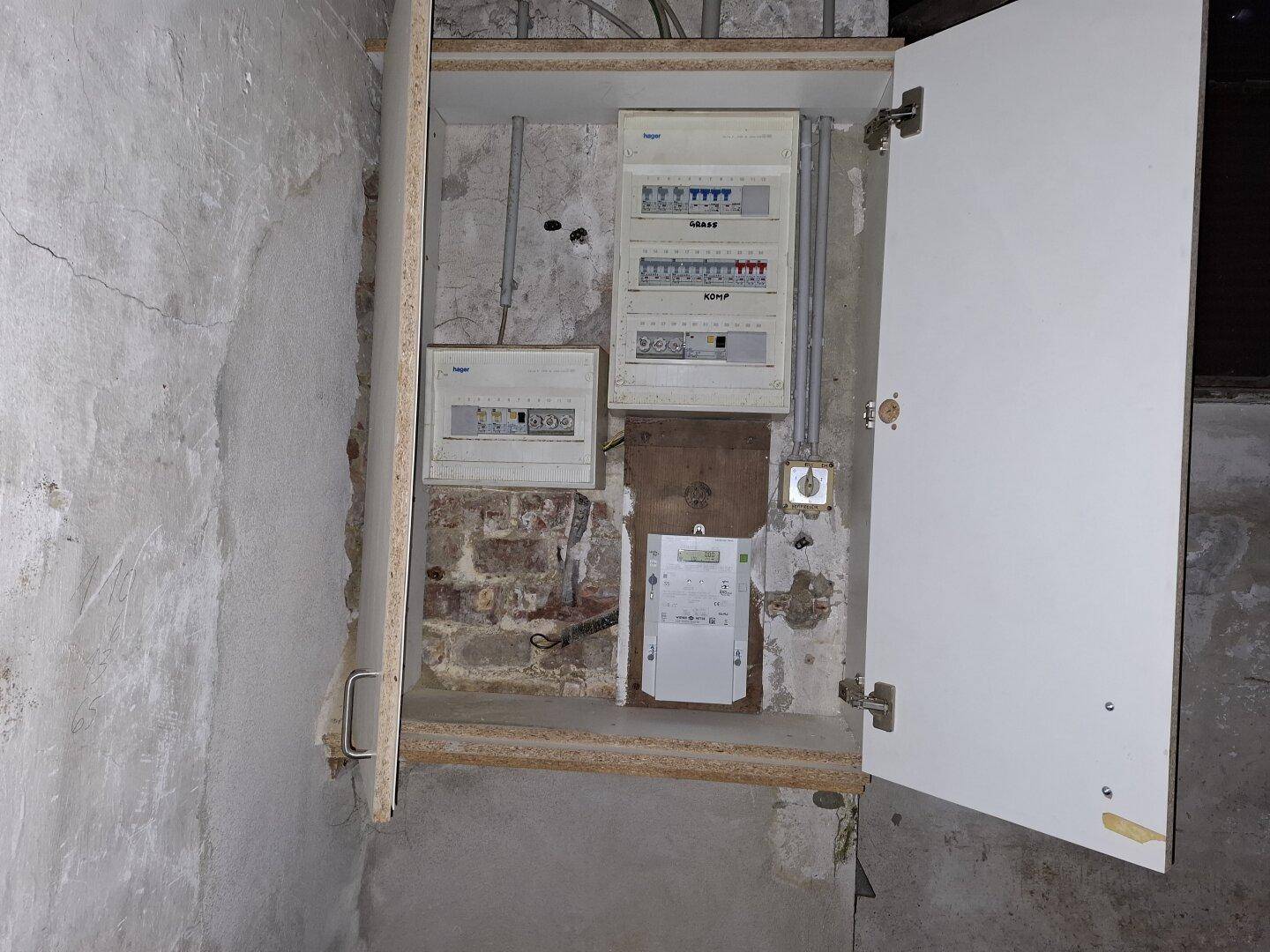 Nahaufnahme eines geöffneten Sicherungskastens mit mehreren Stromzählern und Verkabelungen an einer Wand.