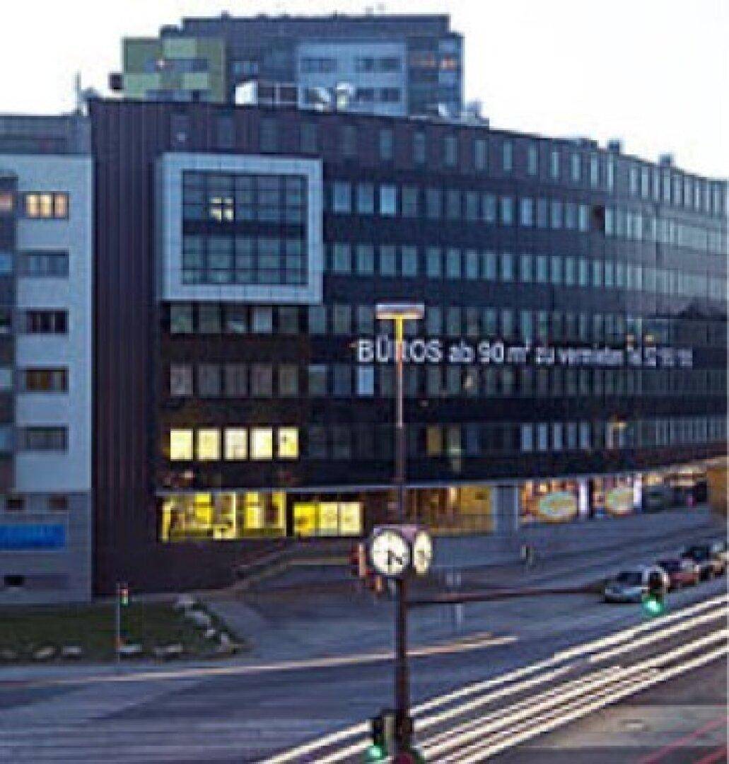 Bürogebäude bei Dämmerung mit beleuchteten Fenstern und Straßenlaternen, an einer belebten Kreuzung.