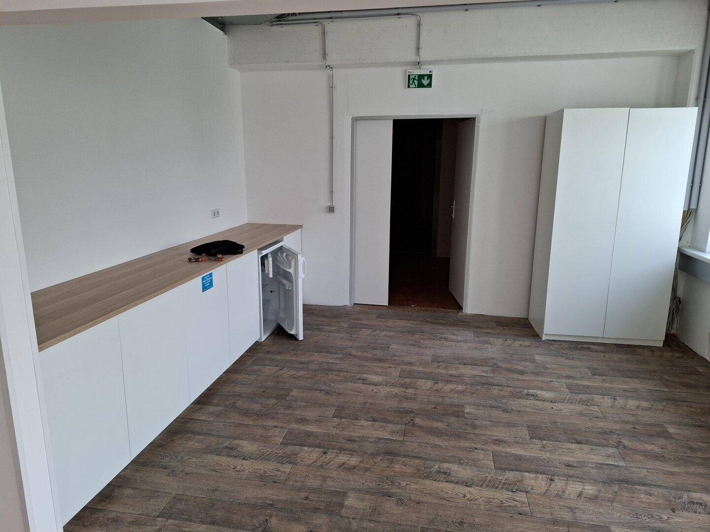 Funktionale Teeküche mit Holztheke, integriertem Kühlschrank und modernem Vinylboden in Holzoptik.