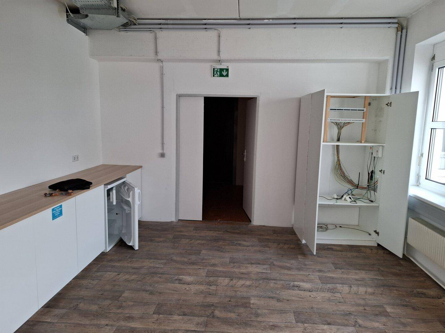 Funktionale Teeküche mit Holztheke, Kühlschrank und offenem Netzwerkschrank in einem modernen Raum.