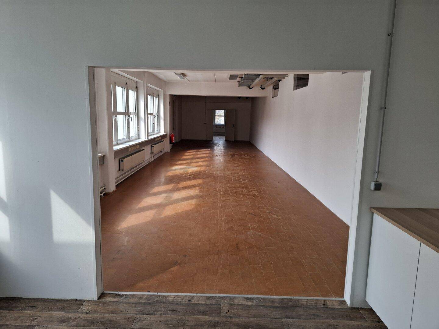 Blick von der Teeküche in den geräumigen, leeren Bürobereich mit viel Tageslicht durch die Fenster.