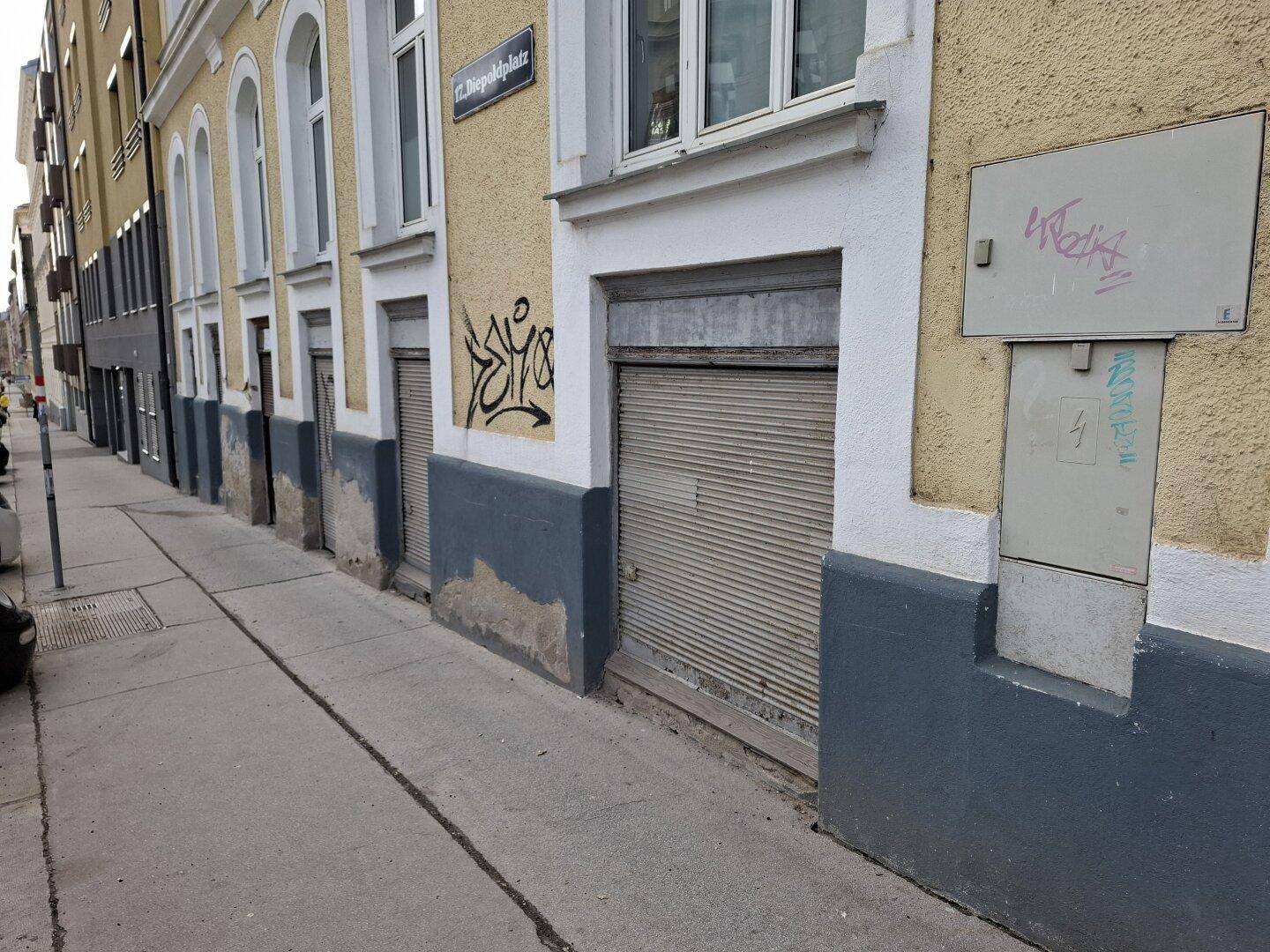 Außenansicht eines Gebäudes mit gelber Fassade, geschlossenen Rollläden im Erdgeschoss und Graffiti an den Wänden.