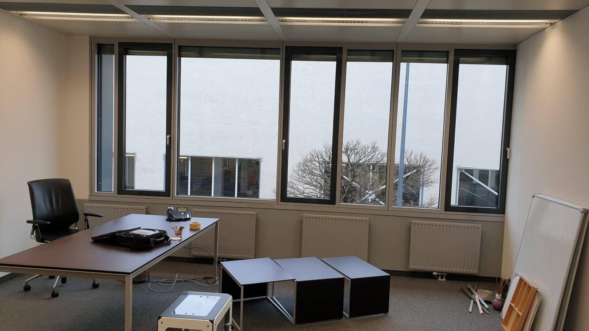 Helles Büro mit großen Fenstern, Teppichboden und einem einfachen Schreibtisch, ideal für konzentriertes Arbeiten.