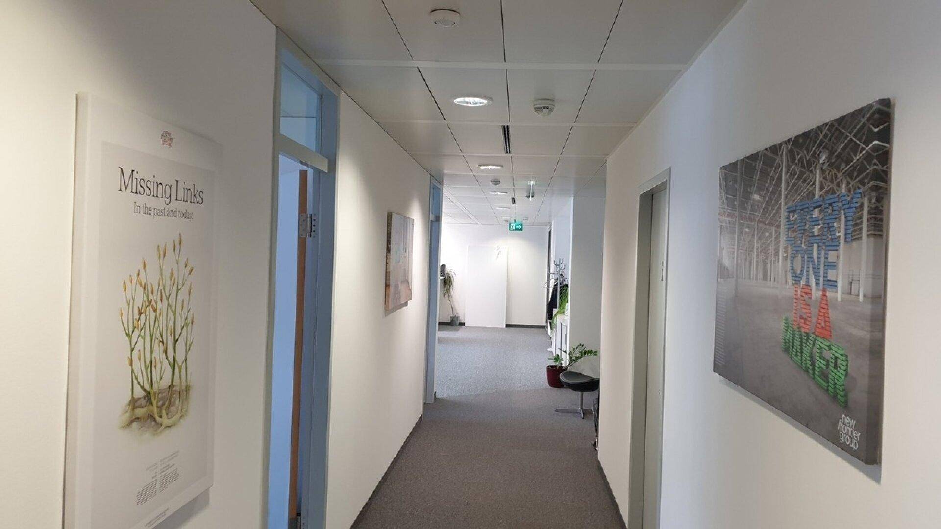 Heller und sauberer Büroflur mit Teppichboden, modernen Kunstwerken und Zugang zu mehreren Büros.
