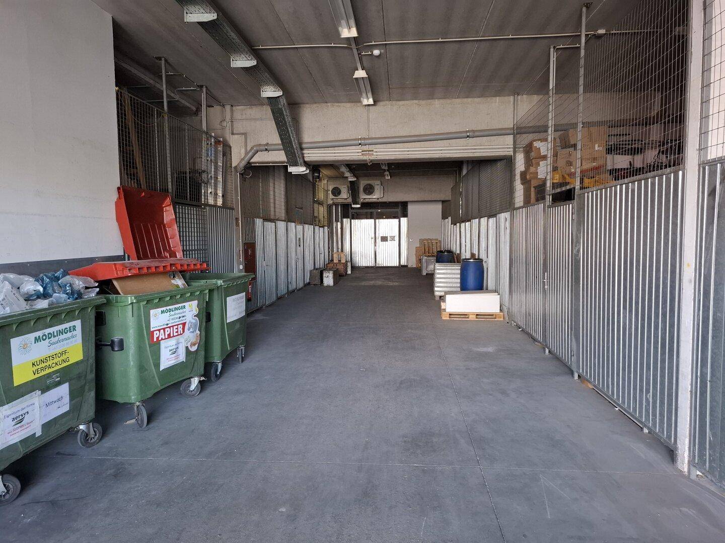 Innenansicht eines Lagerbereichs mit Mülltonnen, Metallzäunen und Betonboden, bereit für die Nutzung.