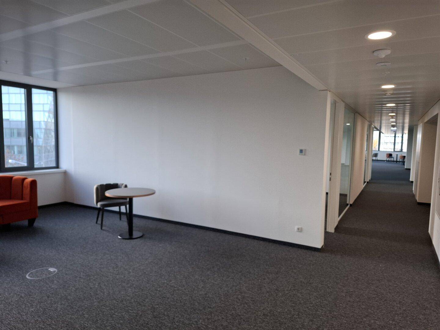 Gemütlicher Loungebereich mit orangefarbenem Sofa und kleinem Tisch, angrenzend an einen langen Flur.