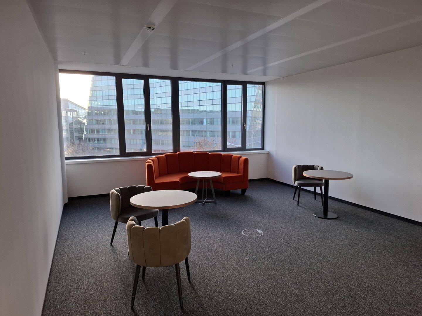 Heller Loungebereich mit bequemen Sitzgelegenheiten, runden Tischen und großen Fenstern mit Stadtblick.