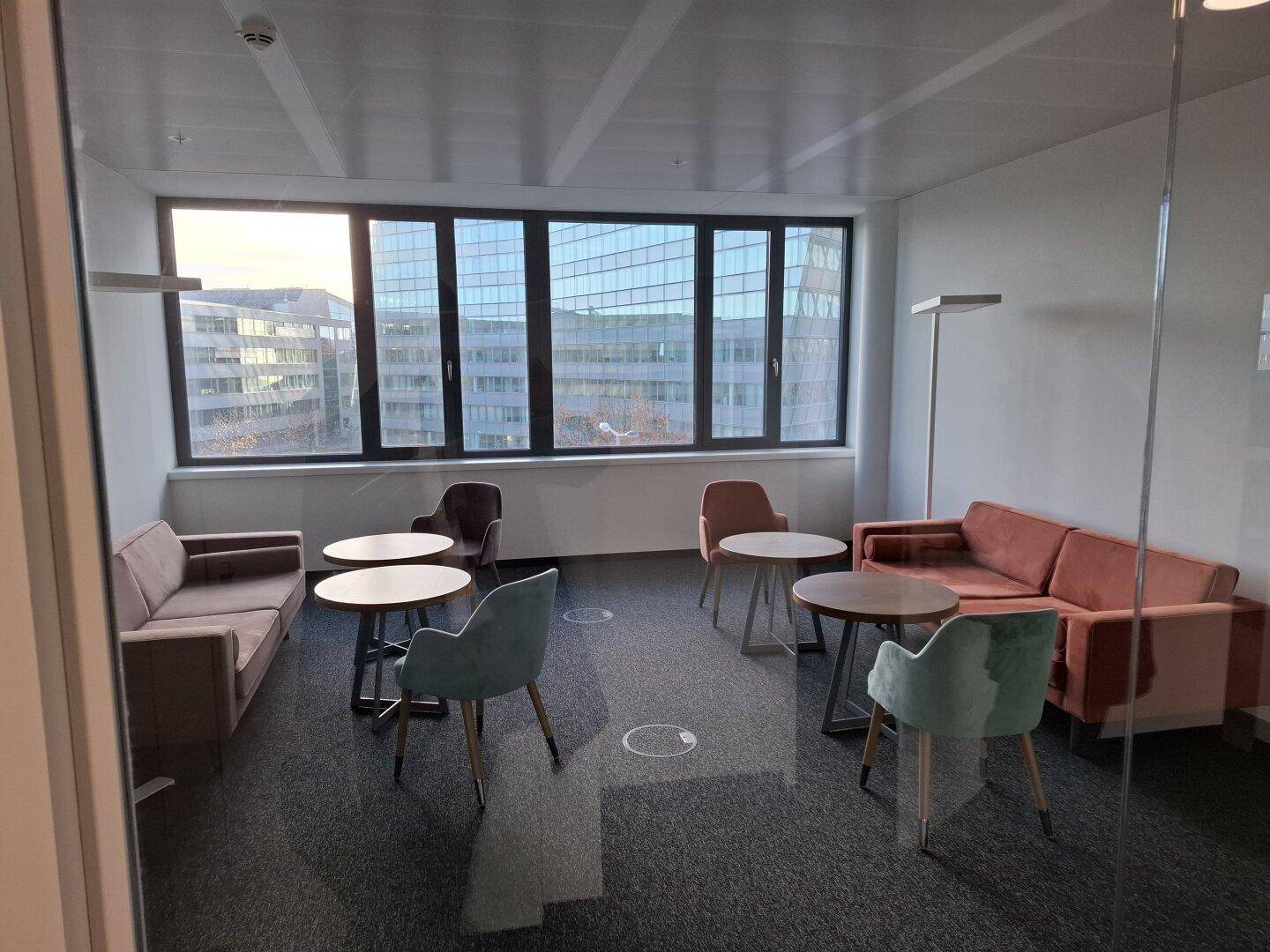 Einladender Loungebereich mit verschiedenen Sofas und Sesseln, runden Tischen und großen Fenstern.