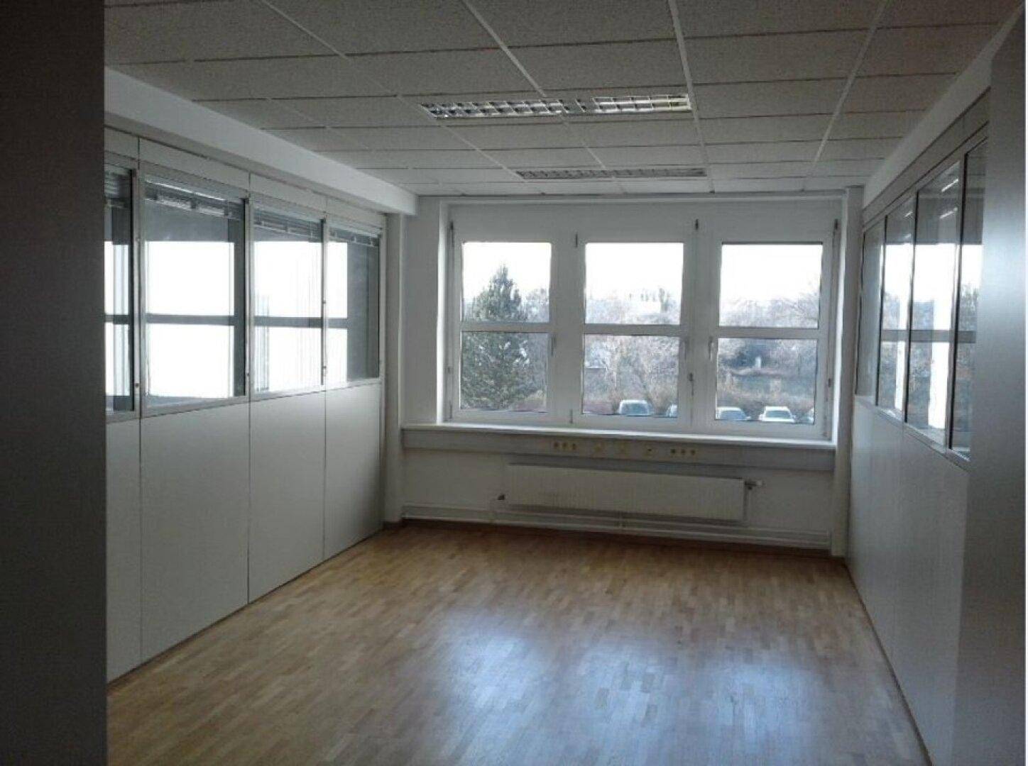 Heller Büroraum mit großen Fenstern, Holzfußboden und abgehängter Decke, ideal für produktives Arbeiten.