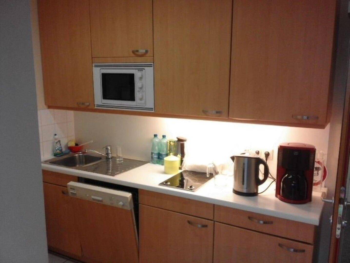 Kompakte Küche mit Holzschränken, Mikrowelle, Spülmaschine und Kochfeld, funktional und gut ausgestattet.