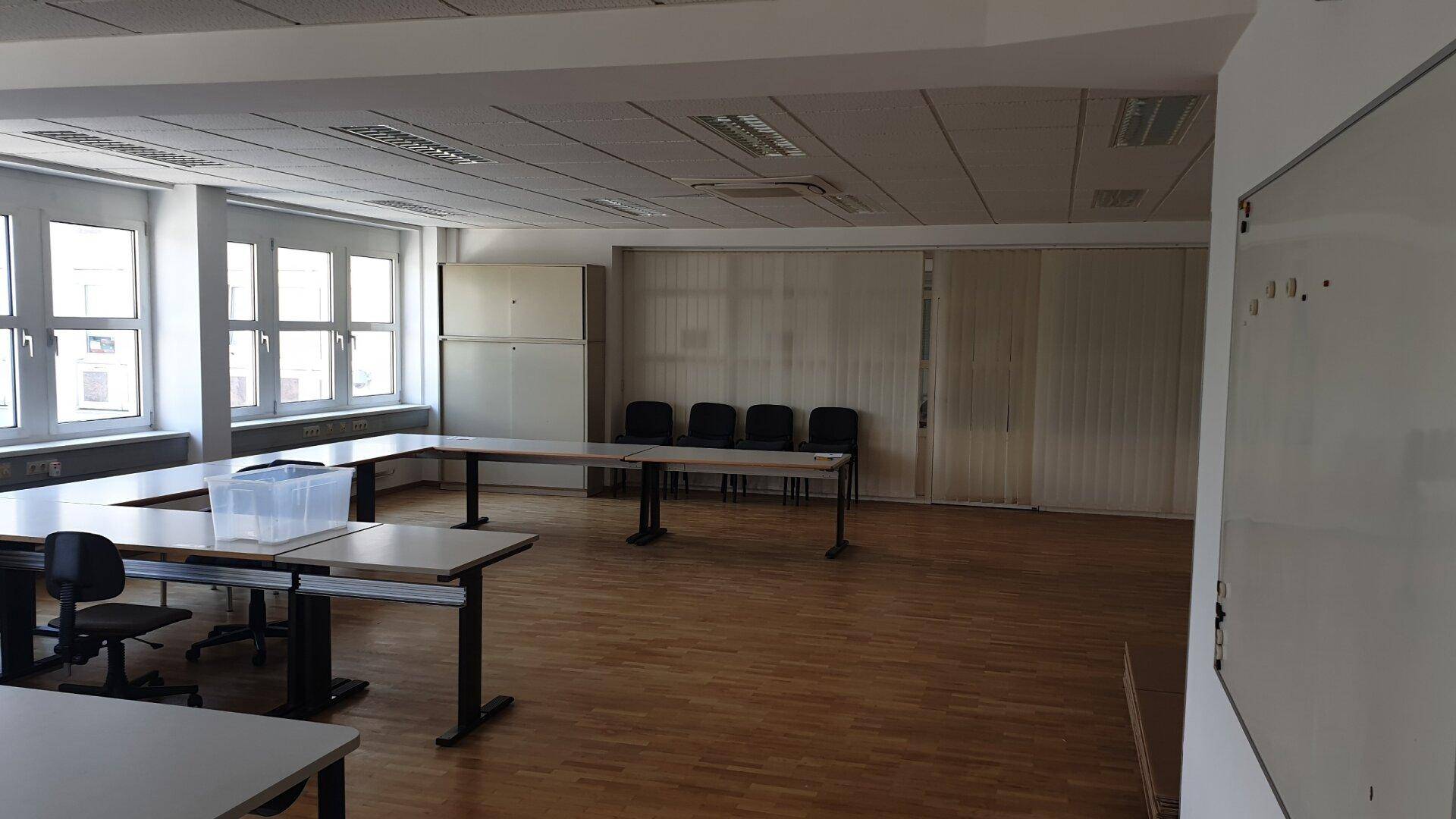 Geräumiger Konferenzraum mit Holzboden, großen Fenstern und flexiblen Tischen für verschiedene Anlässe.